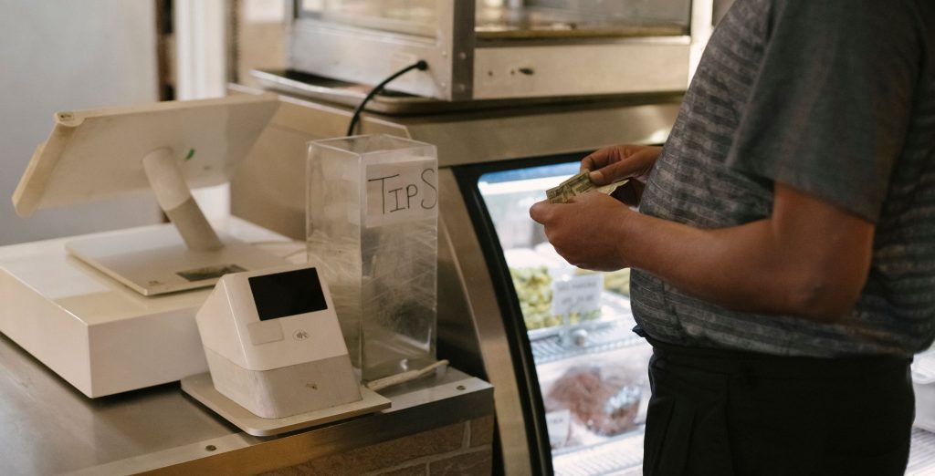 A shopper standing at a supermarket checkout holding banknotes