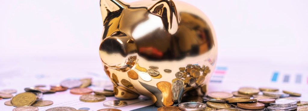 A gold piggy bank standing on financial paperwork with loose coins around it