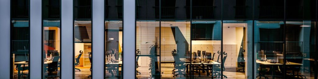 A lit office floor seen through the glass exterior of a modern building at dusk