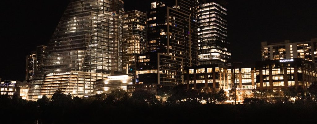 A downtown skyline of lit towers reflected in the river at night